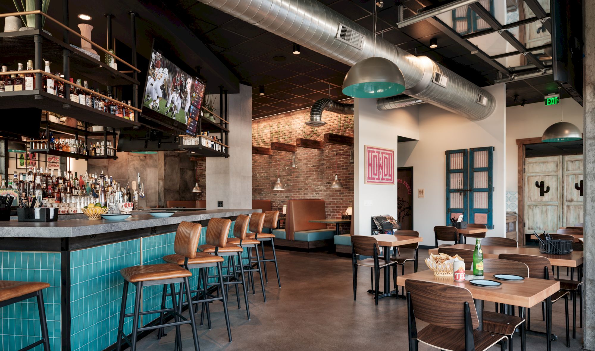 The image shows a modern bar/restaurant with a mix of high stools and tables, a large TV, a fully stocked bar, and contemporary decor ending the sentence.